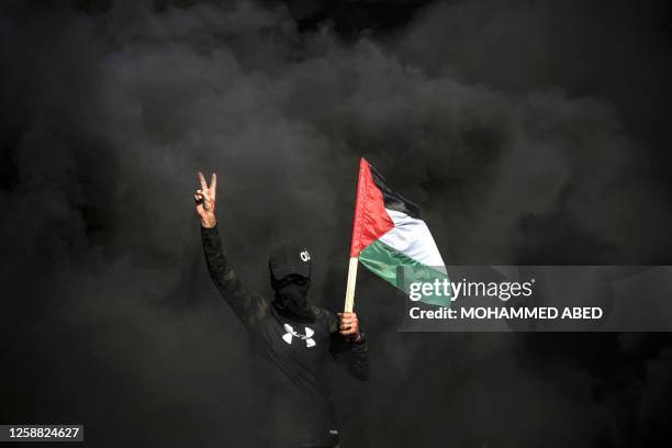 Palestinian youth flashes the victory sign as tyre smoke billows during a protest by the border fence with Israel east of Gaza city on June 19, 2023...