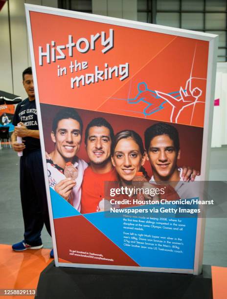 Taekwondo coach Jean Lopez checks out display panels featuring his family as the Taekwondo venue is set up in preparation for competition to begin on...