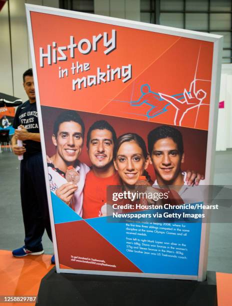 Taekwondo coach Jean Lopez checks out display panels featuring his family as the Taekwondo venue is set up in preparation for competition to begin on...