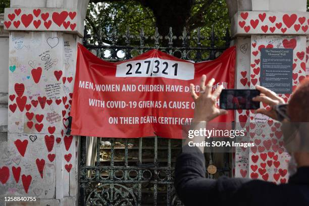 Man takes a photo of a statistics banner at the National Covid Memorial Wall in London.