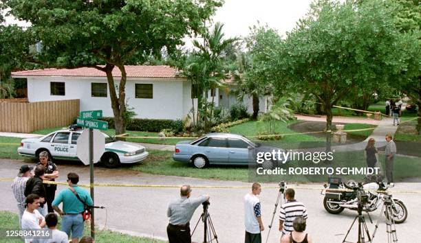 Police investigators, journalists and bystanders stand in front of the perimeter set up by police around the house of a medical doctor who was shot...