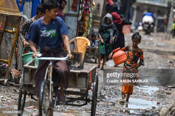 Rohingya refugee girl gestures as she walks through a muddy street at a refugee camp on the World Refugee Day, in New Delhi on June 20, 2023.