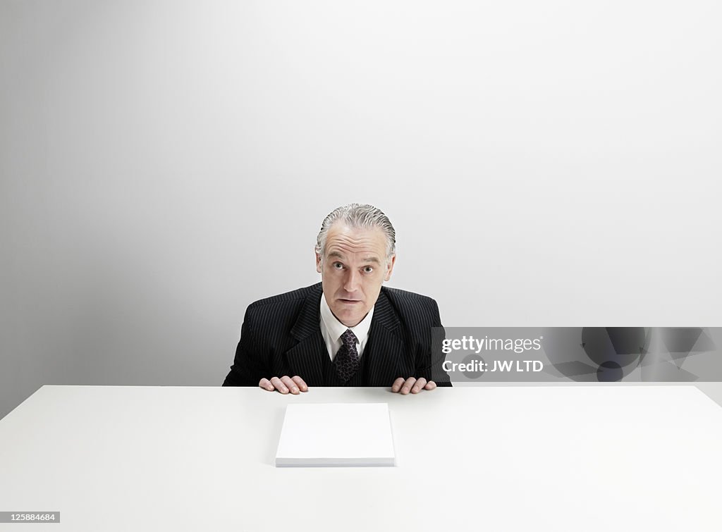 Worried businessman at desk with blank paper 