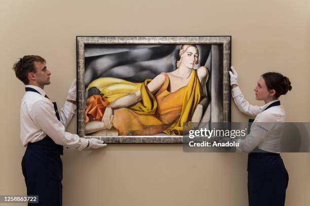 Gallery staff members hold a painting titled âFemme a la robe jauneâ by Tamara de Lempicka during a photocall at Sotheby's auction house showcasing...