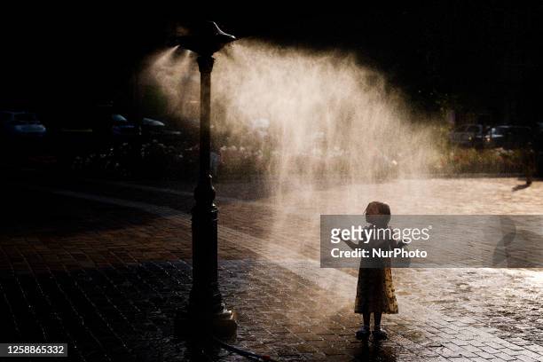 Small girl is cooling by a water sprinkler at the Podgorski Square in Krakow, Poland on June 20, 2023. Hot air masses covered the country and...