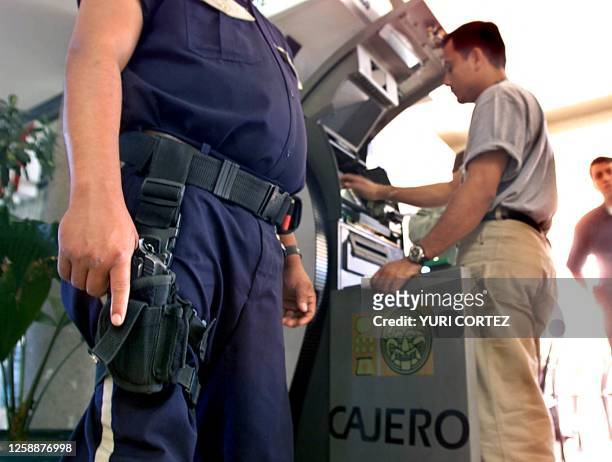 Private security guard protects employees while they load an automatic teller machine with US dollar 01 January 2001, in San Salvador, El Salvador....
