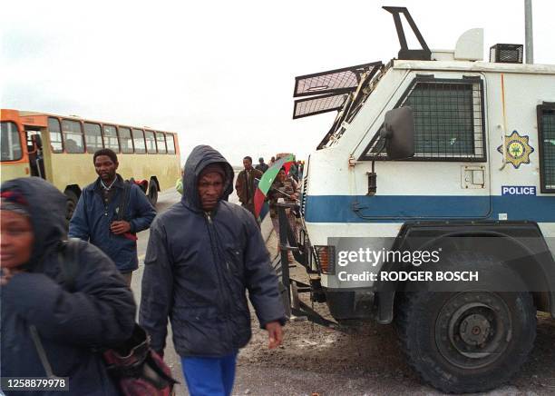 Picture dated 26 May 2000 show commuters getting off the bus in Khayelitsha township outside Cape town and walking past an armoured vehicle belonging...