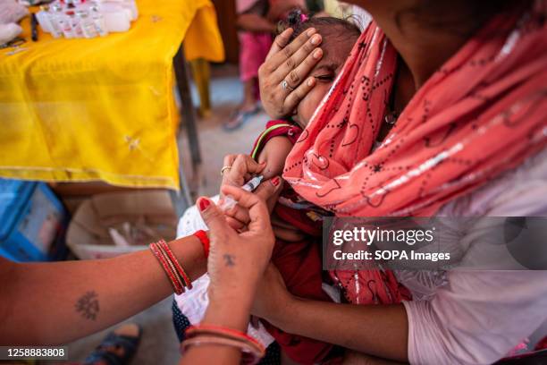 Mother holds a young child while a health worker administers an immunization shot at Anganwadi during a monthly child vaccination camp in Brindaban...