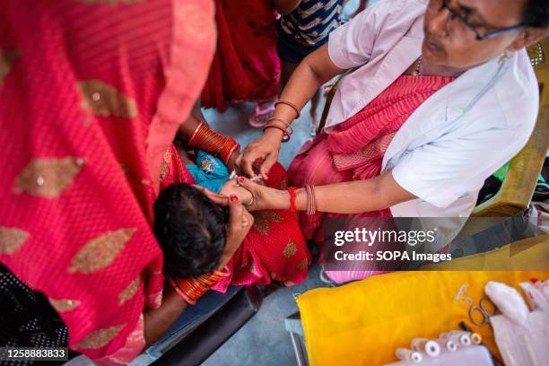 Mother holds a young child while a health worker administers an immunization shot at Anganwadi during a monthly child vaccination camp in Brindaban...