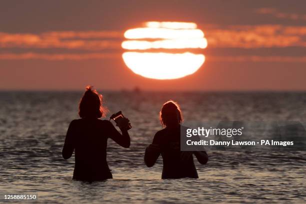 Two woman take a dip in the sea off Cayton Bay in Scarborough as the sun rises on the Summer Solstice. Picture date: Wednesday June 21, 2023.