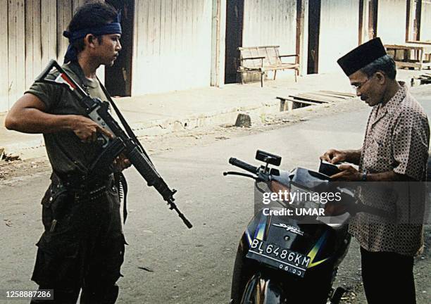 An armed member of the Indonesian elite police force, Brimob, checks the identity of a Achenese man passing an empty street of the subdistrict town...