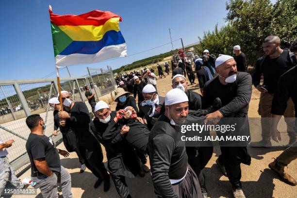 Member of the Druze community holds up their flag as they carry a demonstrator injured during a protest in their village of Majdal Shams in the...