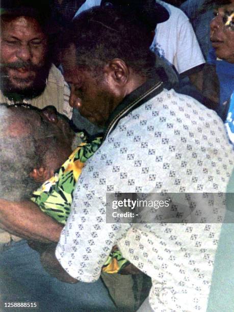 Plainclothes policemen carry the body of Papua pro-independence leader Theys Hiyo Eluay into a waiting ambulance near the border between Indonesia's...