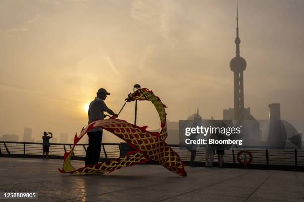 Pedestrian flies a dragon shaped kite along the bund in front of buildings in Pudong's Lujiazui Financial District in Shanghai, China, on Wednesday,...