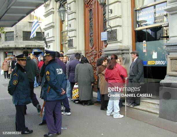 Civilians line up outside an automatic bank teller, guarded by local police, in Montevideo, 02 August 2002. A wave of violent strikes and looting...