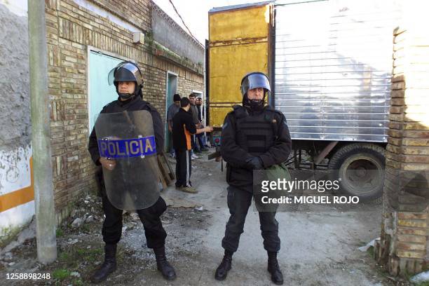 Police guard a truck of food provision as people wait in hopes of receiving food, 02 August 2002 in a district outside of Montevideo. Neighbors of...