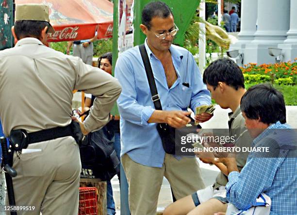 Peddler exchanges dollars on the black market while a police stands by to watch, in Asuncion Paraguay, 18 May 2002. AFP PHOTO/Norberto Duarte Un...