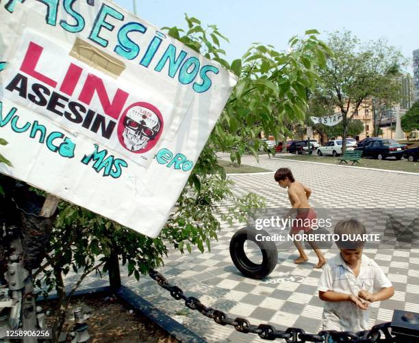 Two children play, 18 September 2002 in the public square of the congress of Asuncion, next to a poster in repudiation against the ex-military...