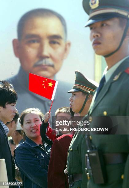 Paramilitary policemen keep an eye on crowds at Tiananmen Square as a flag-waving child is hoisted past a portrait of Sun Yat Sen, considered the...
