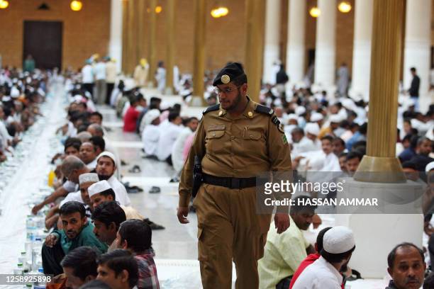 Saudi policeman walks between foreign workers wait to break their fast on the first Friday of Ramadan at the Imam Turki bin Abdullah mosque in...