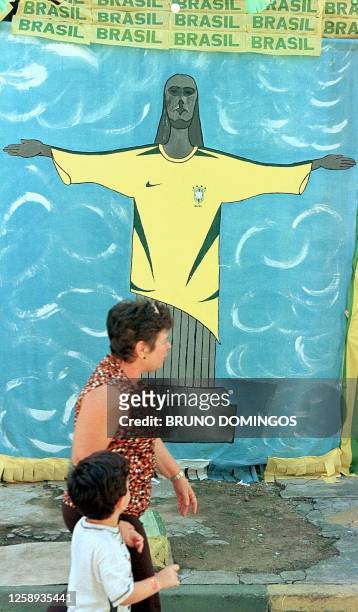 Woman and her son pass in front of a mural painting of Christ representative of Rio de Janeiro, wearing the Brazilian soccer team shirt, 02 June 2002...