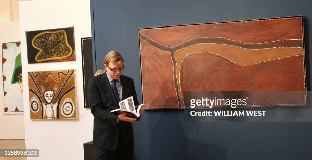 Sotheby's head of Aboriginal Art, Tim Klingender, flicks through a catalogue as he stands next to a painting by famous Aboriginal artist Rover Thomas...