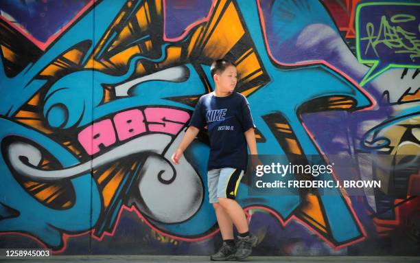 Boy looks back while walking past graffiti on a wall in a street in Beijing on June 30, 2009. Grafitti first penetrated the consciousness of young...