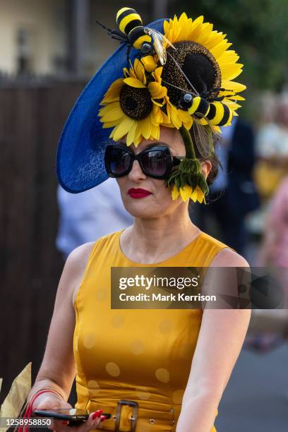 Racegoer wearing a yellow dress and sunflower-and bee-themed hat leaves Royal Ascot on Gold Cup Day on 22 June 2023 in Ascot, United Kingdom. Many...