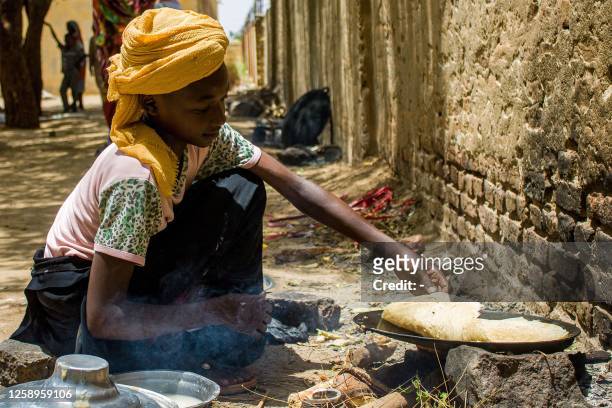 Girl prepares food outside at a camp for the internally displaced in al-Suwar, about 15 kilometres north of Wad Madani, on June 22, 2023. The...