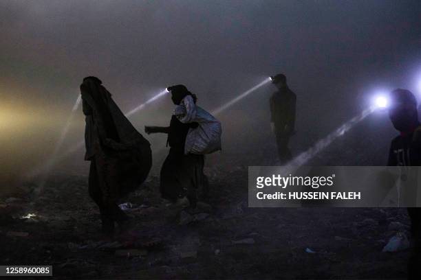 People equipped with searchlights scan for recyclable material for resale at a landfill in Iraq's southern city of Basra late at night on June 22,...