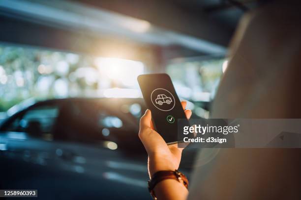 over the shoulder view of young woman using mobile app device on smartphone to order a taxi pick up service in the city - car pooling stock pictures, royalty-free photos & images
