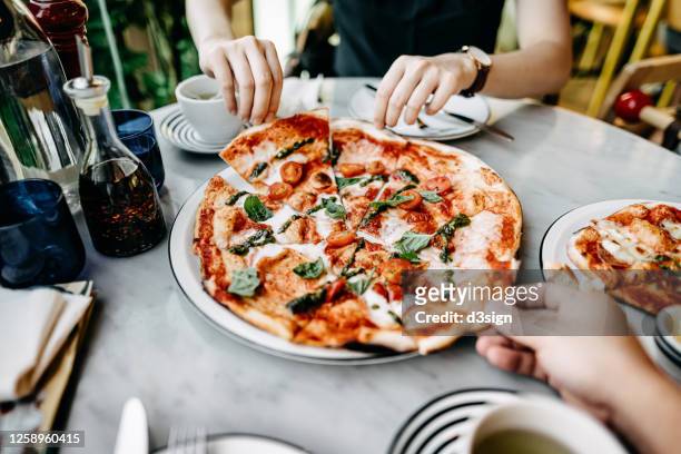 close up of couple getting and sharing slices of freshly made pizza and enjoying meal in an italian restaurant - italienisches essen stock-fotos und bilder