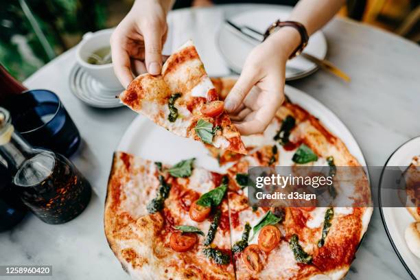 overhead view of woman's hand getting a slice of freshly made pizza and enjoying her meal in an italian restaurant - pizza restaurant stock pictures, royalty-free photos & images