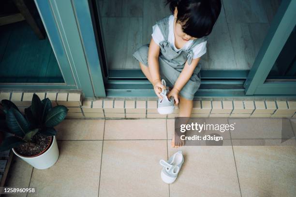 excited and happy little asian girl wearing shoes while sitting on the floor in the garden and getting ready to play outside due to the easing epidemic - child getting dressed stock-fotos und bilder