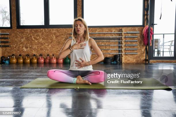 middle life female yoga instructor exercising breathing on an exercise mat at the gym - stomach stock pictures, royalty-free photos & images