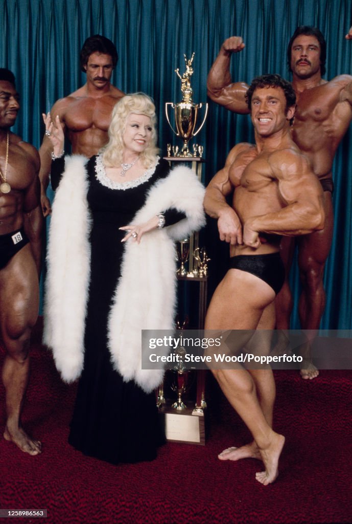 American actress and singer Mae West posing with bodybuilders while American actress and singer Mae West posing with bodybuilders while