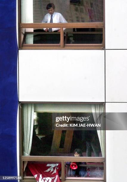 Member of the ruling Millennium Democratic Party looks down to the floor below at their party headquarters building as a woman demonstrator shouts...