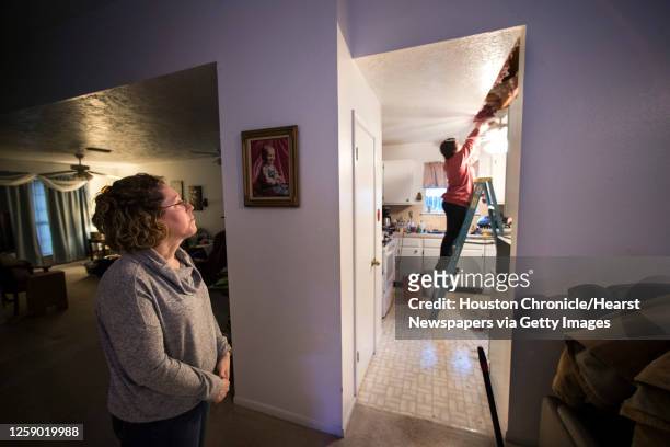 Michelle Toy, left, watches from the living room as Hannah Siqueiros, of HT Innovations, clears insulation from the ceiling after a broken pipe was...