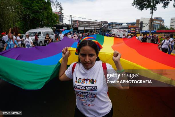 Young woman helping to carry a giant Gay Pride flag at a demonstration as part of the LGBTQIA+ pride parade on June 24, 2023 in San Salvador, El...