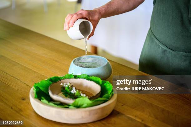 This photograph taken on May 12, 2023 shows a chef preparing the "Fermented lentil pancake , goat kid, salty yoghurt, curry leavesn and wild water...