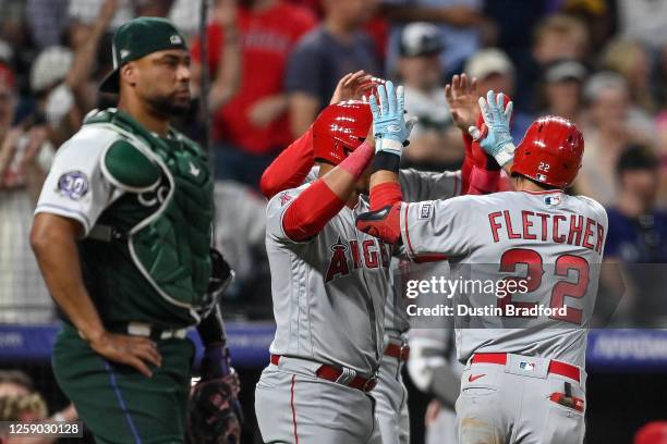 Elias Diaz of the Colorado Rockies looks on as Eduardo Escobar and David Fletcher of the Los Angeles Angels celebrate after a 2-run Fletcher homerun...