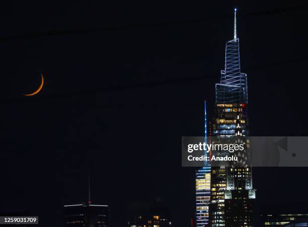 The Moon is seen over the Chrysler and One Vanderbilt buildings in Midtown Manhattan at night from Greenpoint, Brooklyn, New York City, United States...