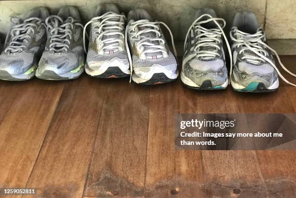 a groupoaa very worn out tennis shoes over a wooden floor. - worn sneakers stock pictures, royalty-free photos & images