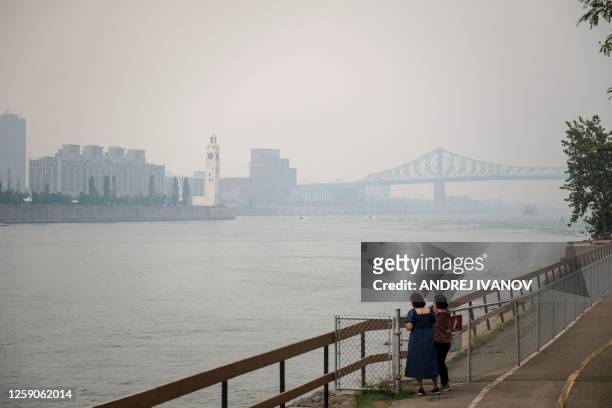 Two women look at the Jacques-Cartier Bridge through the smoke caused by the wildfires in Northern Quebec in Montreal, Quebec, on June 25, 2023....