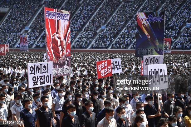 In this photo taken on June 25 residents of Pyongyang hold banners that read "Let us mercilessly beat the puppet group of traitors!", "lackey of...
