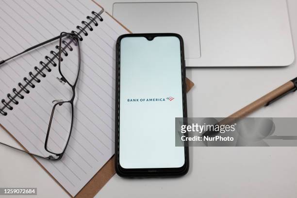 In this photo illustration a Bank of America logo is displayed on a smartphone screen above a notebook next to glasses and a pen in Athens, Greece on...