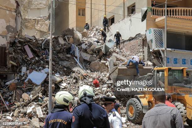 Civil defence first responders speak with a policeman at the scene of a collapsed 13-storey-building in the Sidi Bishr district of Egypt's northern...