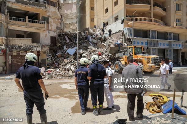 Civil defence first responders speak with a policeman at the scene of a collapsed 13-storey-building in the Sidi Bishr district of Egypt's northern...