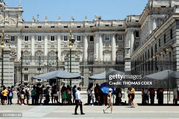 Tourists protect themselves of the sun while they queue to visit the Royal Palace in Madrid city centre under very high temperatures, on June 26,...