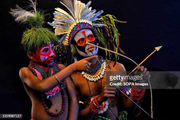 An artist and his son pose with an Arrow and their faces painted as part of their Impersonating Act on the theme of different Tribal Cultures. For...